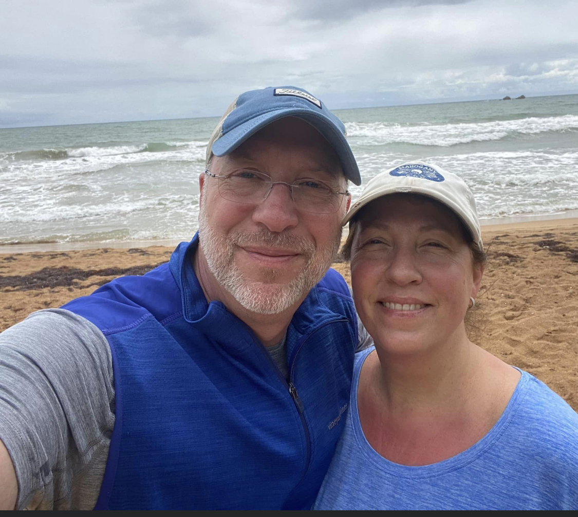 A photo of 2 people taking a selfie together on a beach. The man is named Matt, and the woman is named Carrie,